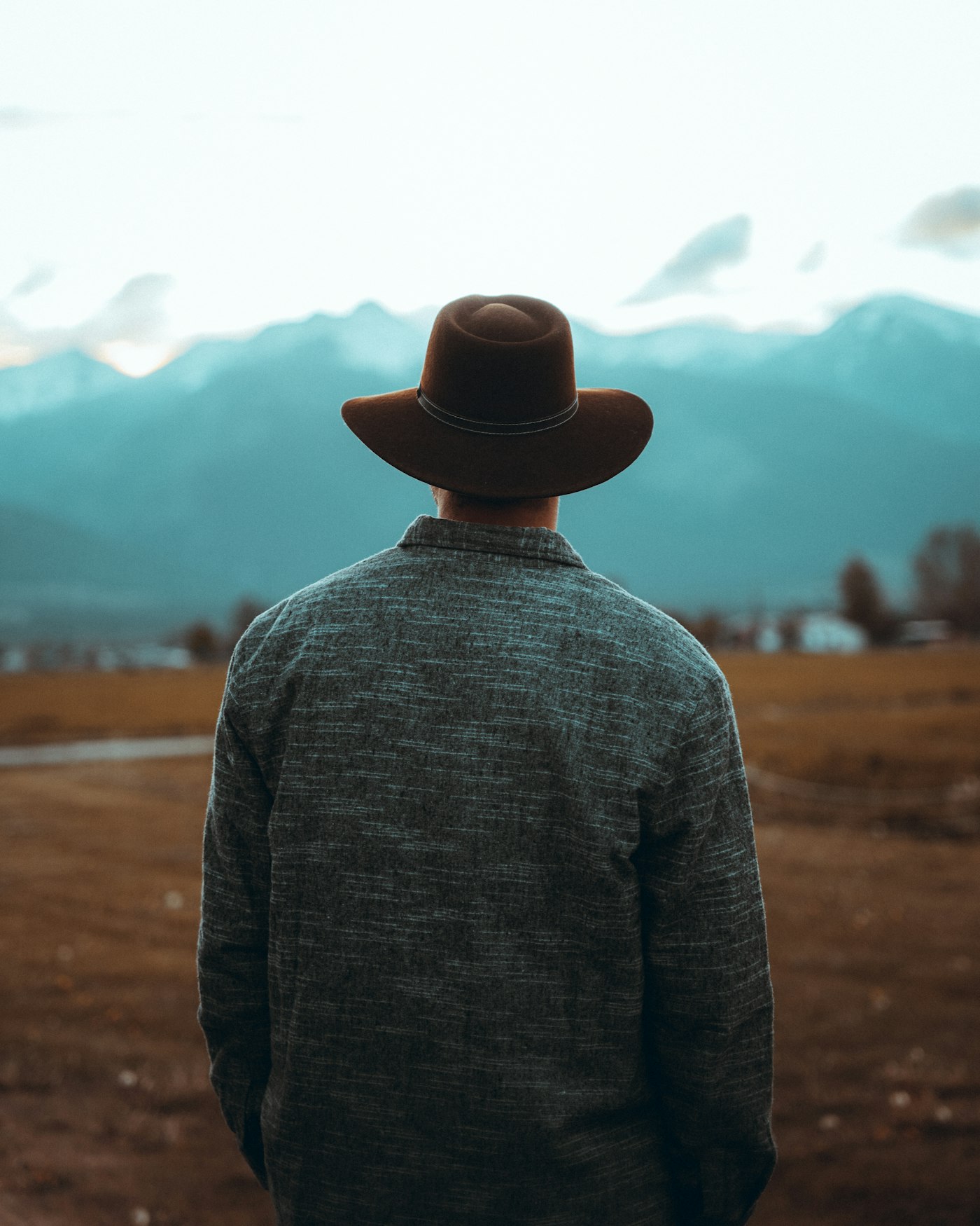 A person seen from behind wearing a hat, looking toward the mountains